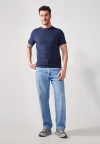 Mørkeblå kortermet ribbestrikket t-skjorte kombinert med lyseblå rette jeans. Overtøyet fullføres med grå joggesko.