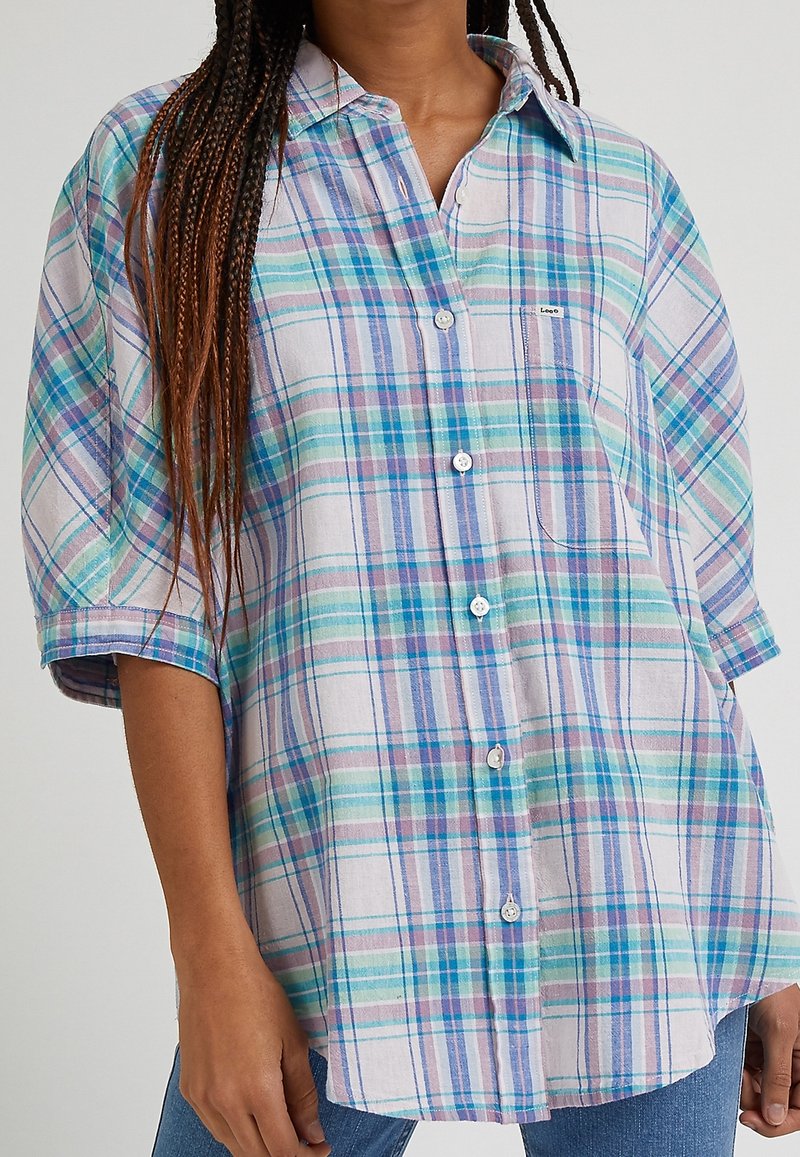 Camicia a maniche corte in tessuto a quadri con una vestibilità ampia. Presenta strisce blu, verde e viola, taschino sul petto e bottoni bianchi.