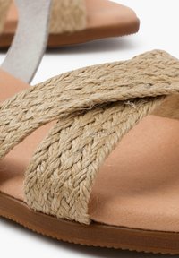 Płaskie sandały z plecionymi paskami z naturalnego włókna w kolorze beżowym, gładką wkładką w odcieniu brązowym oraz lekką gumową podeszwą.