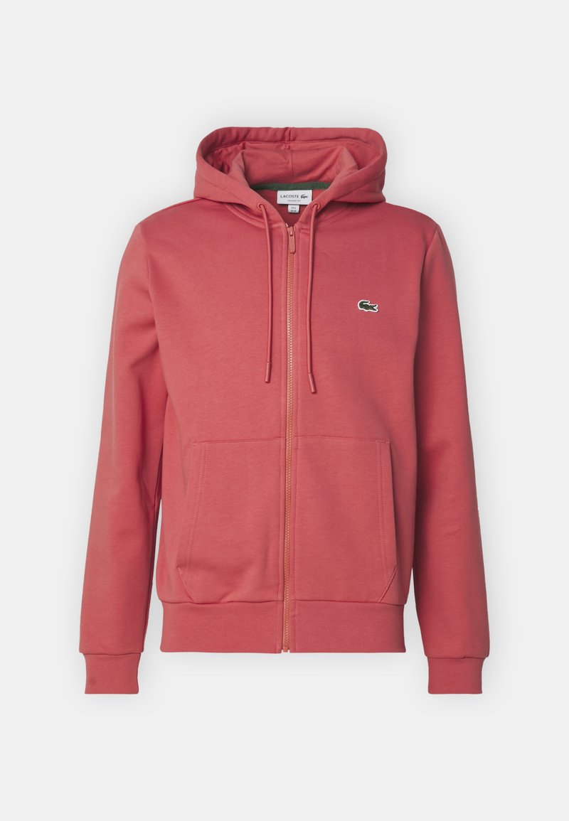 Sweatshirt à capuche zippé rouge en tissu doux, doté d'une poche kangourou et d'un petit logo vert Lacoste sur la poitrine gauche.