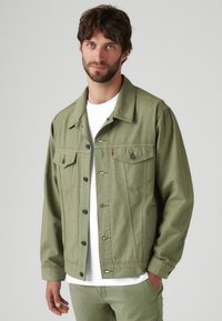 Jachetă din denim verde măsliniu cu închidere buton, două buzunare pe piept și o croială lejeră. Purtați peste un tricou alb, cu detalii de cusătură subtile.