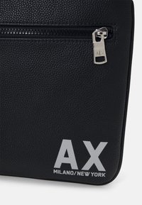 Borsa in pelle nera texture con zip argentata, caratterizzata da un logo bianco prominente "AX MILANO/NEW YORK" nell'angolo in basso a destra.