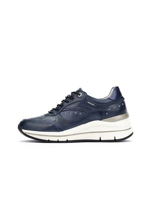 Zapatilla de piel azul marino con puntera redondeada, tachuelas decorativas y una suela blanca en contraste con un acento plateado. Diseño con cordones.