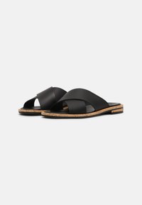 Sandales en cuir noir avec des brides croisées, semelle en liège et design plat. Présentent une texture lisse et un style minimaliste.