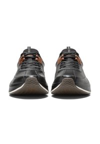 Schwarze Sportschuhe mit einem glatten Lederoberteil, strukturierten Details, braunen Schnürsenkeln und einer Gummisohle mit einem gewellten Muster.