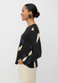 Zwarte langemouwen shirt met abstracte beige en marineblauwe patronen, gemaakt van zacht materiaal, gecombineerd met lichtgekleurde broeken.