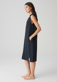 Sleeveless navy dress with pockets, featuring a straight silhouette and a side slit. Material appears smooth and lightweight.