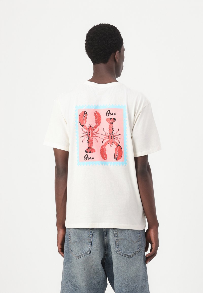 Tricou alb din bumbac cu un graphic colorat de homar pe un fundal roz asemănător unui timbru poștal, situat pe spate. Mâneci scurte, croială lejeră.