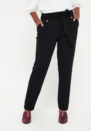 Pantalons noirs avec une taille ceinturée, des poches latérales et des accents de bouton. Texture lisse et design de jambe fuselée. Assortis à des chaussures à imprimé serpent rouge.