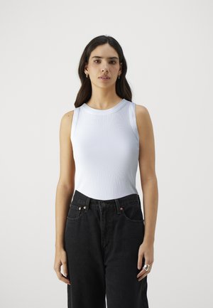 White ribbed sleeveless top paired with high-waisted black denim jeans. The top features a round neckline and fitted design.