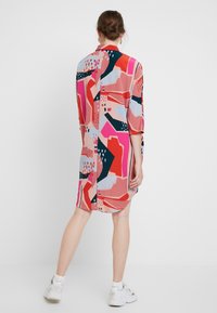 Robe colorée jusqu'aux genoux avec des motifs abstraits en rose, marine et bleu clair. Fabriquée dans un tissu lisse avec une coupe décontractée.