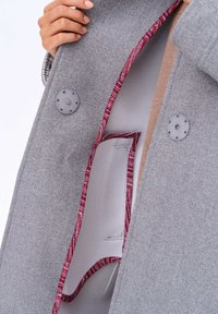 Manteau en laine gris avec des boutons ronds gris, doublure bordeaux contrastante et une texture intérieure douce ornée de motifs complexes.
