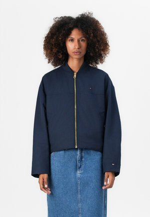 Navy bomber jacket with a gold zipper, relaxed fit, and elastic cuffs. Features a small logo on the chest and seamless pockets.