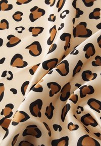 Tessuto in stampa leopardata con uno sfondo beige adornato da macchie a forma di cuore nere e marroni, caratterizzato da una texture liscia e morbida.