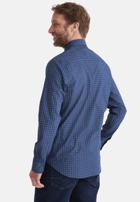 Herrenbluse in Blau mit einem kleinen, sich wiederholenden weißen Muster, langen Ärmeln, spitzem Kragen und abgerundetem Saum. Aus einer Baumwollmischung.