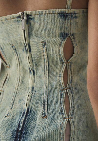 Denim korsett i lys blå med mørkeblå sprut. Har glidelås i front og utskjæringer langs sidene med kontraststing.