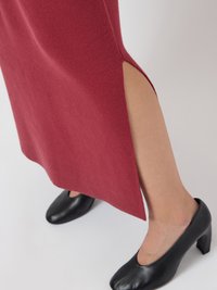 Roter Rock mit seitlichem Schlitz bis zum Oberschenkel, kombiniert mit schwarzen flachen Schuhen, die das Unterschenkel vor einem neutralen Hintergrund zeigen.