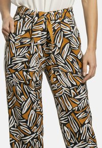 Pantalones estampados con un diseño atrevido de formas blancas y ámbar sobre un fondo negro; la cintura atada y los bolsillos laterales añaden funcionalidad.