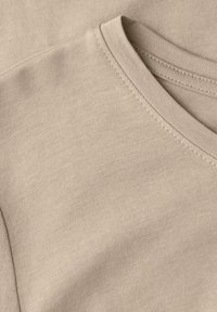 Béžová bavlněná tričkovina s výstřihem do V a jemným šitím. Hladká textura s rovnoměrným vazbou.