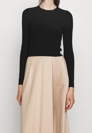Maglietta nera a maniche lunghe a coste abbinata a una gonna beige con pieghe su un lato. Focus sui contrasti di texture e sul design lineare.