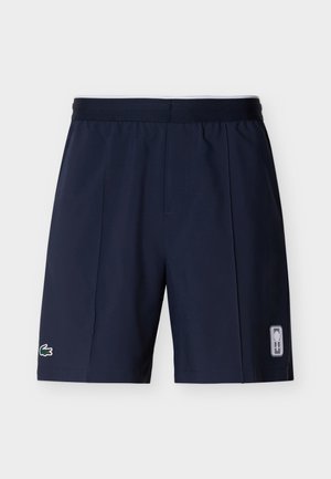 Tumesinised spordipüksid elastse vöökohaga, vasakul jalal Lacoste krokodilli logo ja paremal jalal ristkülikukujuline graafika.