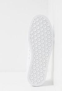 Biała płócienna trampka z sześciokątną, teksturowaną gumową podeszwą, z metalowymi przelotkami i prostym, minimalistycznym wzornictwem.