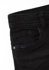 Jeans de mezclilla negra con un bolsillo frontal, trabillas y costuras en contraste. La tela presenta un ligero desgaste y una textura suave.