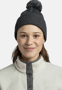 Gray knitted beanie with a pom-pom on top, featuring a ribbed texture. Worn over a cream fleece jacket with gray button detailing.