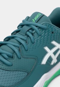 Blauer Sportschuh mit strukturiertem Obermaterial, weißem Logo und grünen Akzenten; verfügt über flache Schnürsenkel und eine gepolsterte Zunge für Komfort.