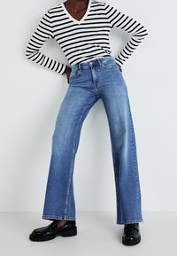 Striped black and white long-sleeve top, blue wide-leg jeans, and black loafers. Smooth fabric, casual design, visible stitching and hardware.