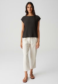 Donkergrijze, gestructureerde, kortekousen top, gecombineerd met loszittende, lichtbeige broek. Model staat blootvoets en laat een eenvoudig ontwerp zien.