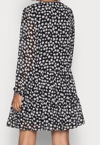 Schwarzes langärmliges Kleid mit floralem Muster, ausgestattet mit einem stufigen Rock und transparentem Stoff. Die Blumenfarben sind Weiß und Hellrosa auf dunklem Hintergrund.