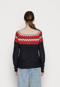 Neulepaita, jossa on pyöreä pääntie ja kontrastikuviot punaisena, kermanvärisenä ja mustana, siirtyen tummansiniseen vartalon osalla.