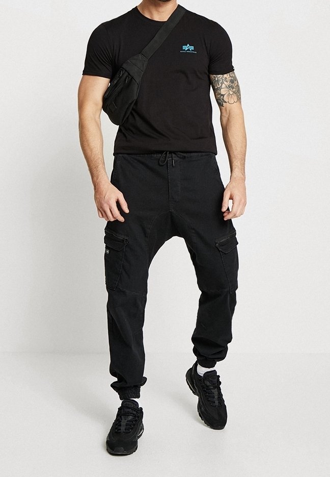 T-shirt noir avec logo bleu, pantalon cargo noir avec poches zippées, baskets noires et sac bandoulière noir. Style décontracté.