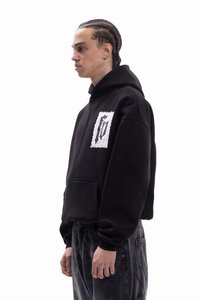 Sudadera negra con capucha, bolsillo delantero y un parche gráfico blanco con un diseño negro. Puños y dobladillo acanalados, ajuste relajado.