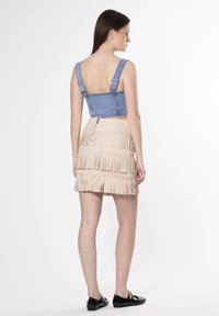 Denim crop top met verstelbare bandjes; beige leren franjeskirt met gelaagde textuur en ritssluiting aan de achterkant; zwarte schoenen.
