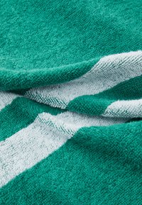 Serviette turquoise avec une surface texturée, ornée de rayures blanches et en tissu doux et absorbant. Les plis créent de la profondeur et de la dimension.