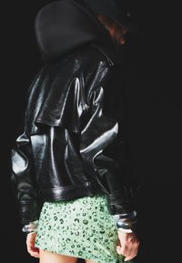 Černá umělá kožená bunda s vrstveným designem, kombinovaná s mini sukní v mentolové barvě pokrytou flitry a stříbrnými náramky.