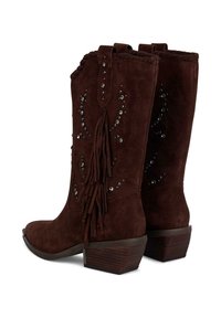 Botas de vaquero de ante marrón con flecos decorativos, adornadas con tachuelas plateadas, puntera afilada y un tacón de madera apilada.