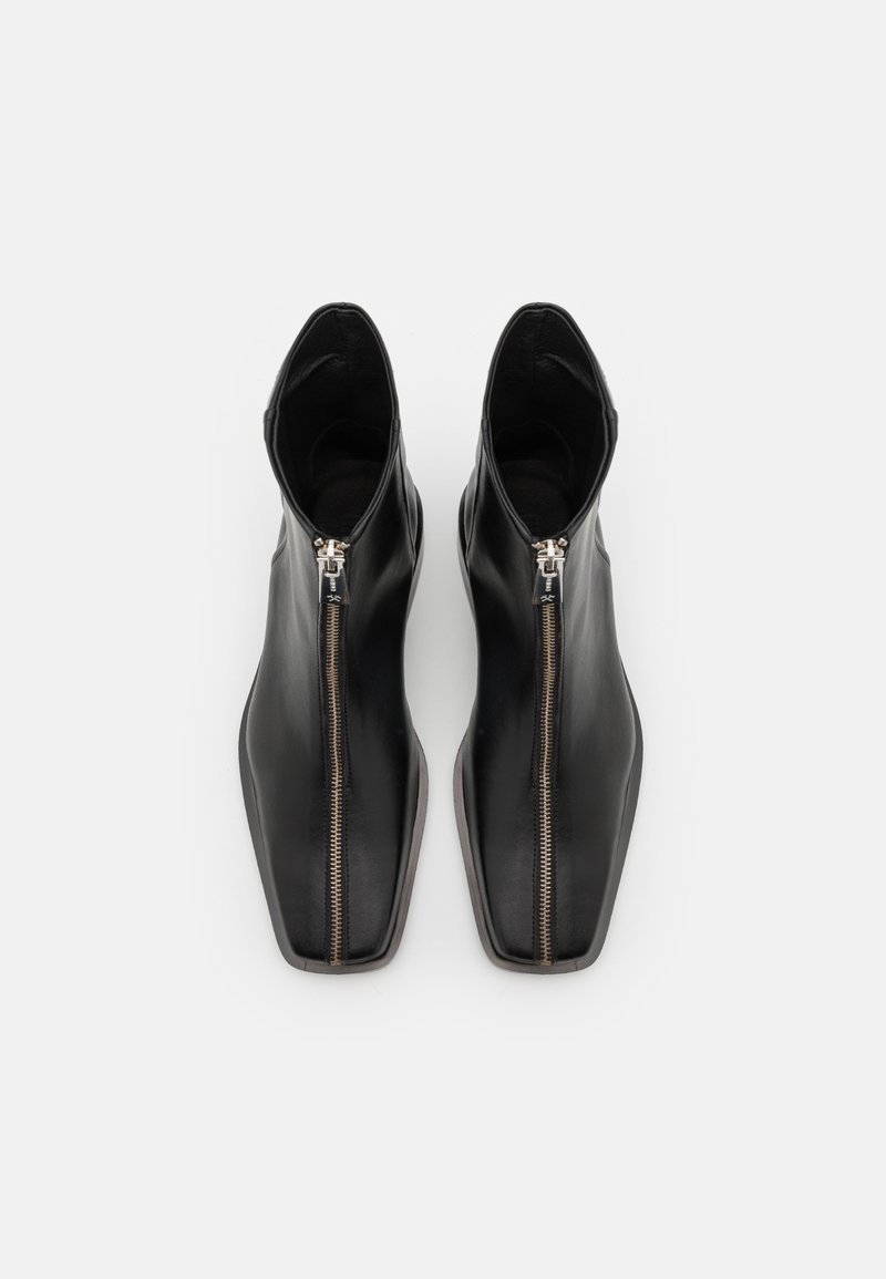 Schwarze Lederankelstiefel mit spitzer Zehenform und seitlichen Reißverschlüssen, die eine glatte Textur und ein minimalistisches Design aufweisen.