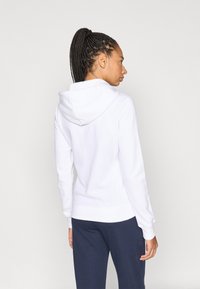 Λευκό φούτερ με κουκούλα και κορδόνι, μακριά μανίκια και ριμπ μανσέτες· συνδυασμένο με μπλε σκούρο παντελόνι· μαλακή υφή και καθημερινός σχεδιασμός.