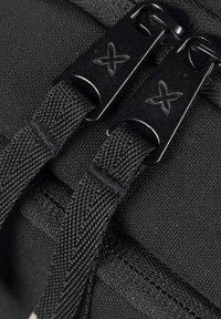 Sac à dos en tissu noir en gros plan, présentant des zippers lisses, des cordons tressés, et un matériau texturé avec des coutures renforcées.