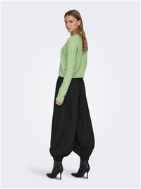Zeleni pleteni džemper, crne široke hlače i crne čizme s petom. Džemper ima meku teksturu; hlače imaju elastične manžete i prostrani kroj.