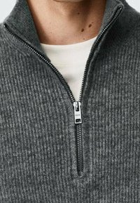 Grauem Reißverschluss-Pullover mit geripptem Stoff und hohem Kragen. Verfügt über einen metallenen Reißverschluss und ein weißes Rundhals-T-Shirt darunter.