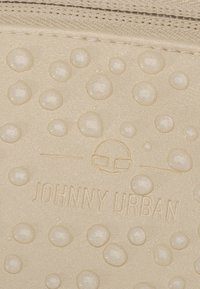 Beige textúrájú anyag, kiemelkedő pöttyökkel és vízcseppekkel. A "JOHNNY URBAN" felirattal és szemüveget ábrázoló logóval van ellátva.