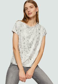 Błyszcząca srebrna bluzka z krótkim rękawem o luźnym kroju, z delikatnym wzorem teksturowym, zestawiona z szarymi dżinsami.