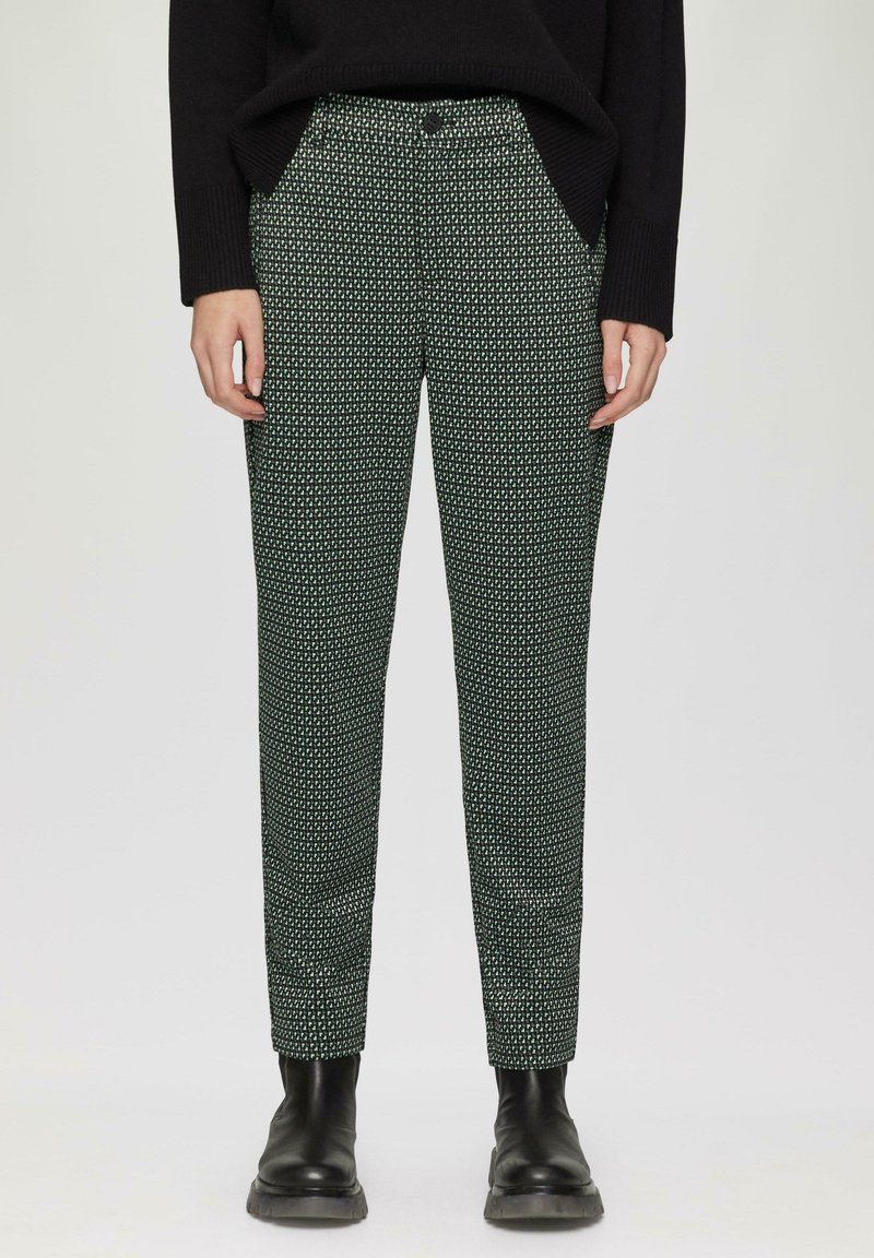 Pantalons à motifs verts présentant un design géométrique, coupe slim, poches et fermeture à bouton, associés à des bottines noires.