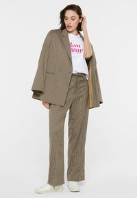 Oversized plaid blazer in beige and brown, paired with a white graphic t-shirt, matching plaid trousers, and white sneakers.