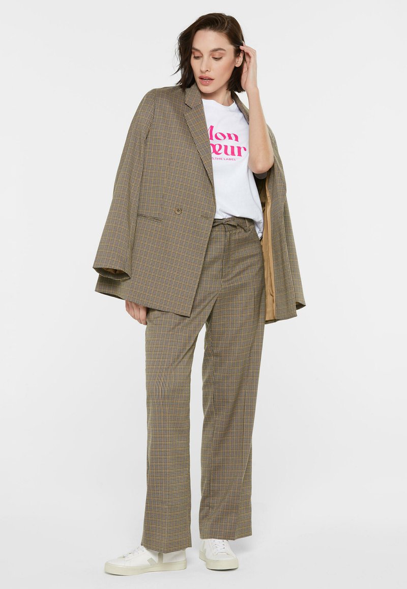 Oversized plaid blazer in beige and brown, paired with a white graphic t-shirt, matching plaid trousers, and white sneakers.