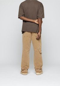 T-shirt marron surdimensionné et pantalon cargo beige avec poches, vu de dos. Le pantalon présente un tissu texturé et une coupe décontractée.